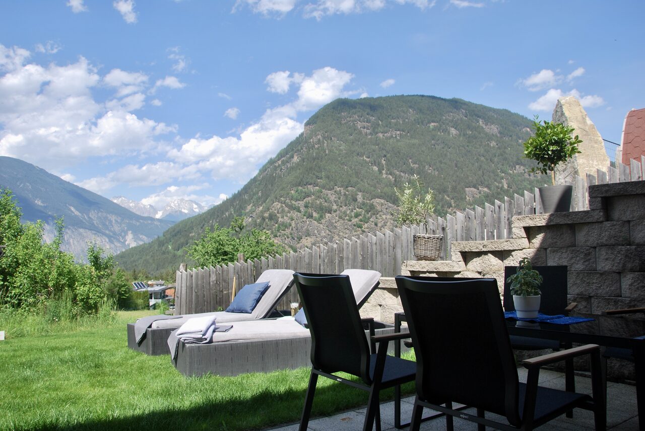 Terrasse mit Esstisch und Stühlen vor einer Natursteinmauer, dahinter der Blick ins Tal.
